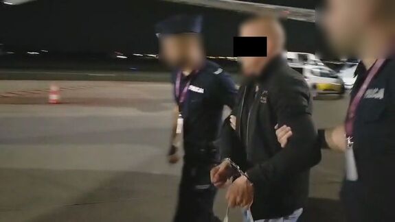 Policjanci wyprowadzają zatrzymanego mężczyznę z samolotu i prowadzą do radiowozu.