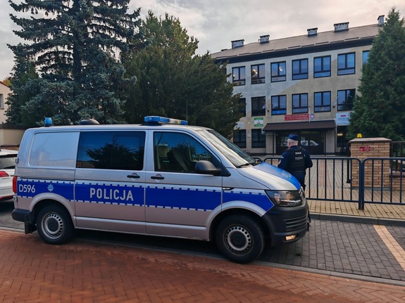 przed szkołą stoi radiowóz policyjny i policjant